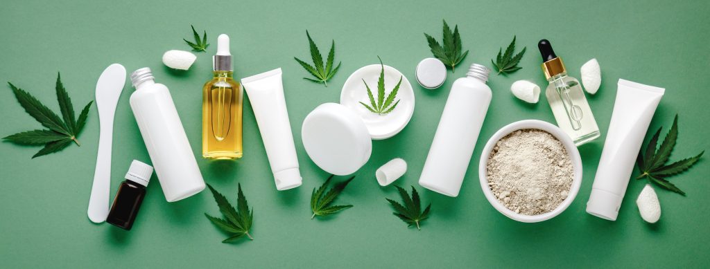 Set of hemp skin care cosmetics in white mockup packaging. Moisturizing cream, Serum, lotion, CBD oil, essential oil cannabis leaves. Flat lay long web banner copy space. on green background